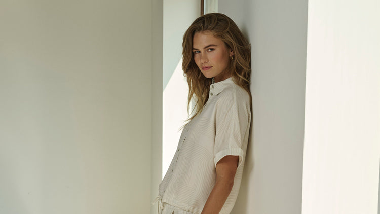 Person wearing a light-colored outfit standing in a minimalistic indoor setting.